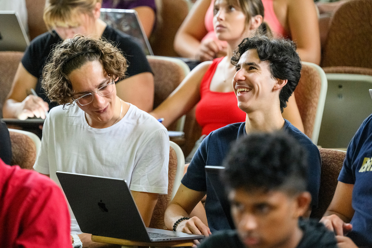 Students sit in a lecture hall smiling.