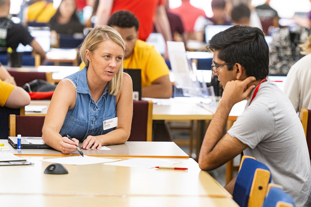 A staff member sits at a table with a student engaging in a conversation.