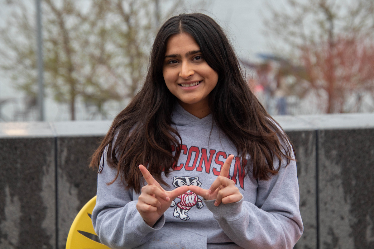 Student sitting on a Memorial Union chair holds up the Wisconsin "W."