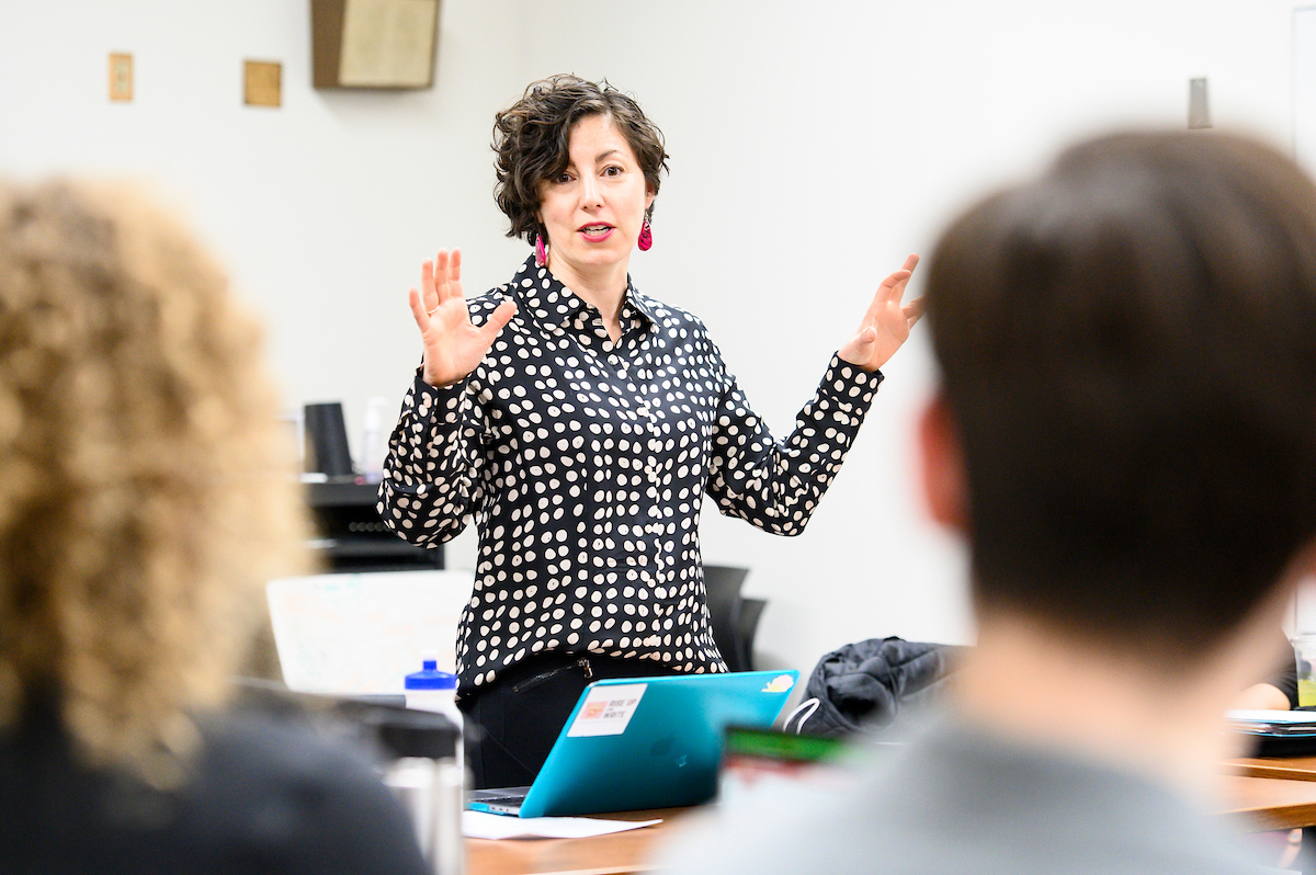 A staff member stands at the front of a lecture hall speaking to an audience.